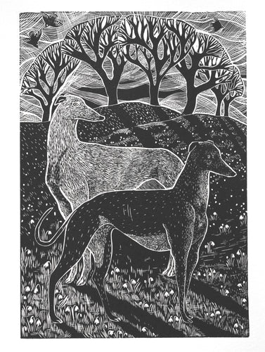 A black and white hand printed linocut art print depicting two greyhounds amidst snowdrops, with tree silhouettes in the background.